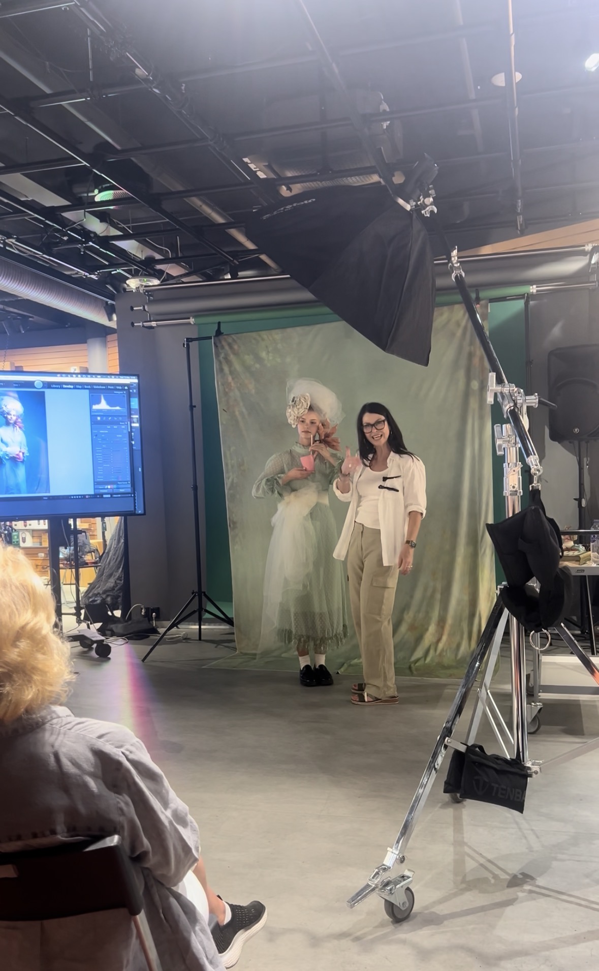 Martina standing with a model in a green backdrop setup, reviewing images on screen